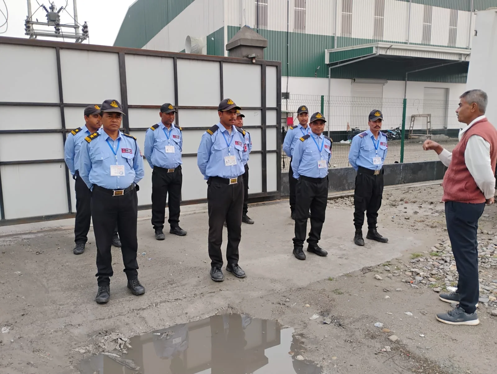 DNSMS guards in uniform standing at attention during a daytime briefing outside a client site gate in Guwahati