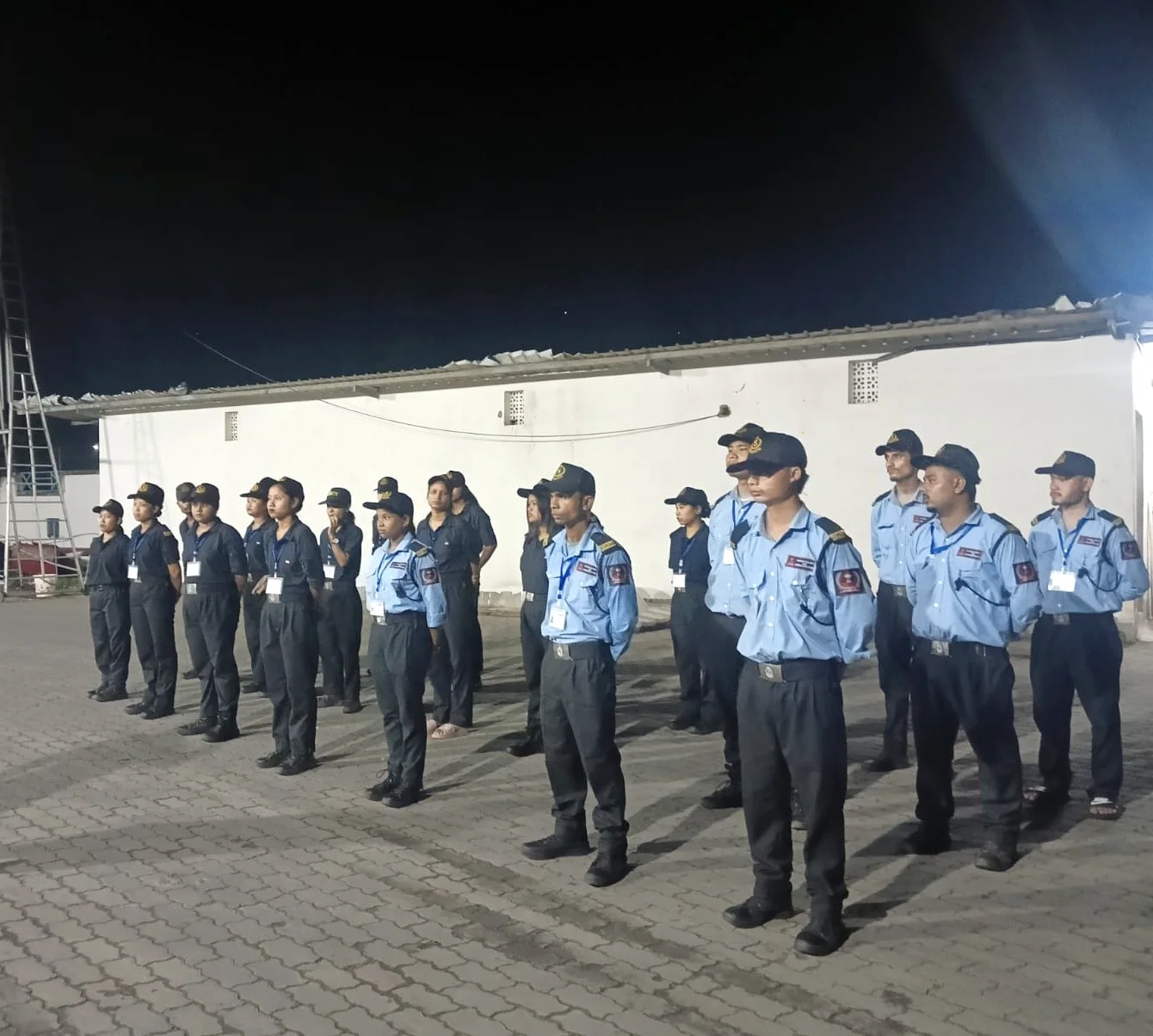 DNSMS security guards in sky-blue and navy uniforms standing in formation at night under floodlights in Guwahati
